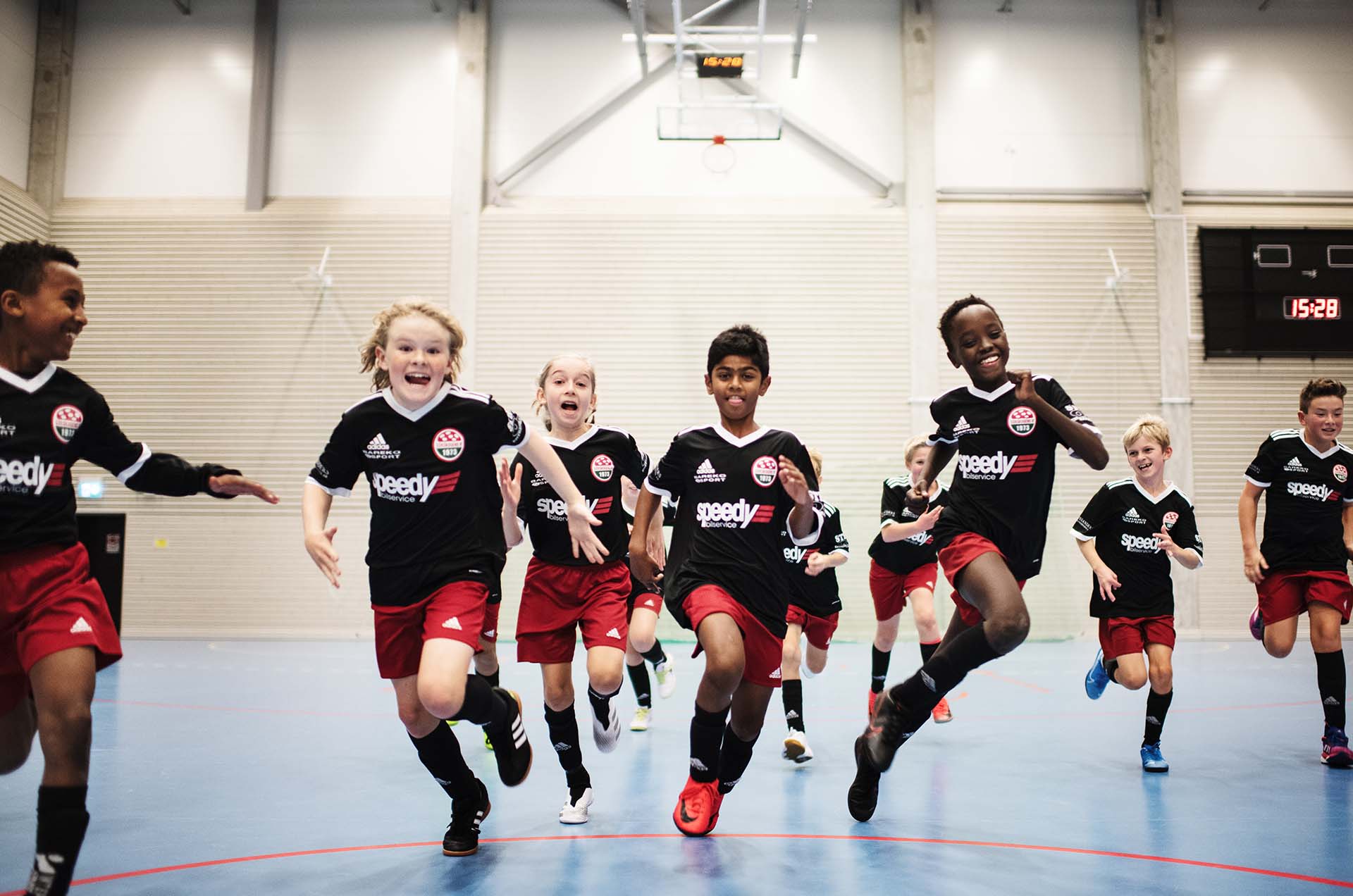 Barn i idrottskläder springer i sporthall.