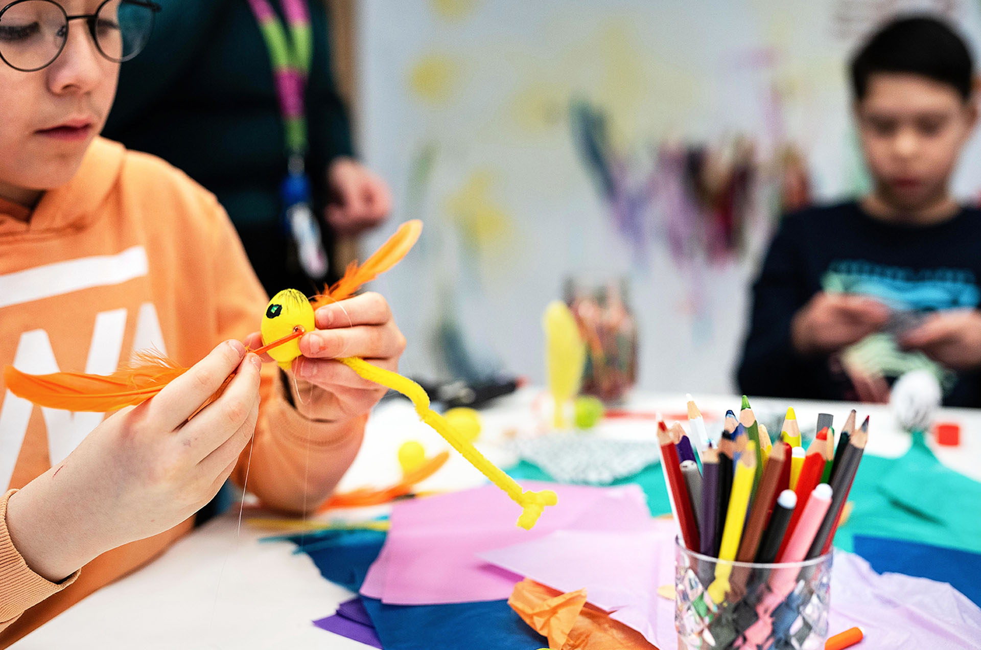 Två barn pysslar vid ett bord med färgglada papper och pennor.